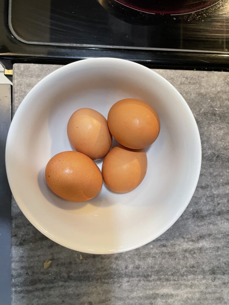 Four eggs in a white bowl on the counter.