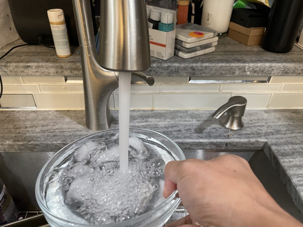 Filling glass bowl with water and ice.
