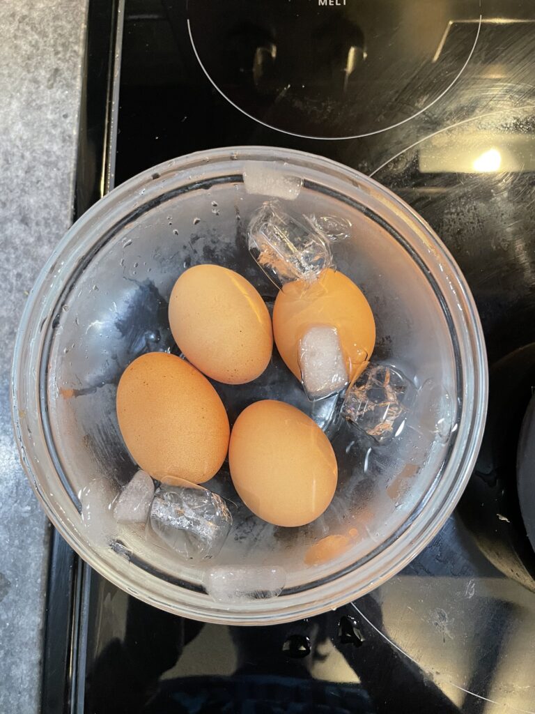 Four eggs in a glass bowl filled with water and ice.