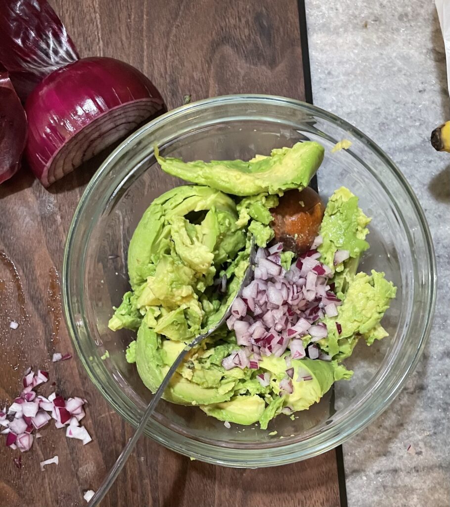 Chopped onions in place on top on avocados. In a clear bowl on top of a brown cutting board.