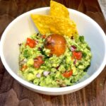Garlic Jalapeno Guacamole in a white bowl, and 2 chip and avocado pic on top.