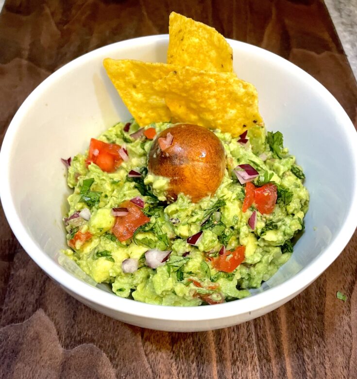 Garlic Jalapeno Guacamole in a white bowl, and 2 chip and avocado pic on top.