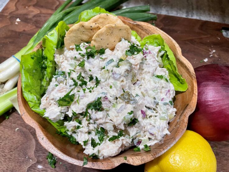 Best chicken salad recipe in a wodden bowl. On top of a cutting board with lemon next to an onion, and a green onion on the other side.