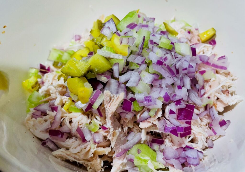 Added red onions, celery, and pickles to the bowl with the shredded chicken.