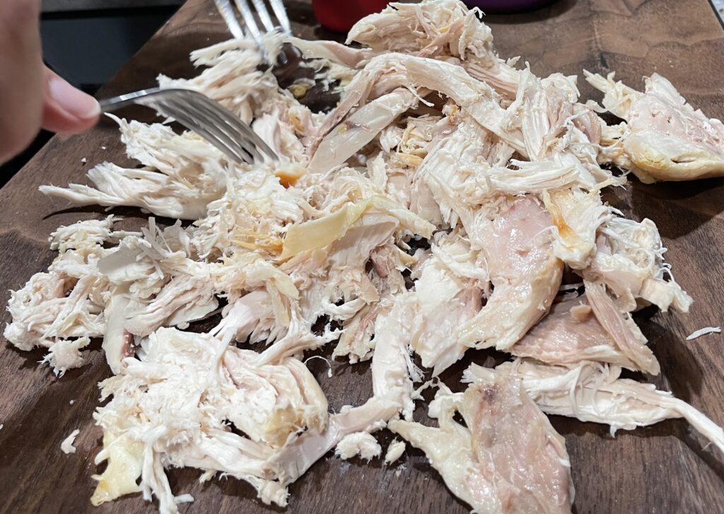 Shredding chicken on cutting board with forks. 