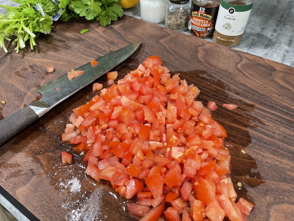 Chopped tomatoes on a brown cutting board. Knife next to it.