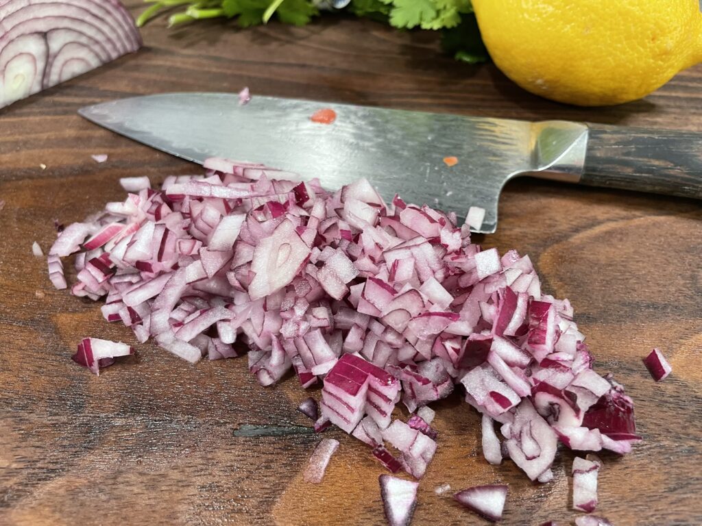 Chopped onions on a brown cutting board. There is a knife next to the onions