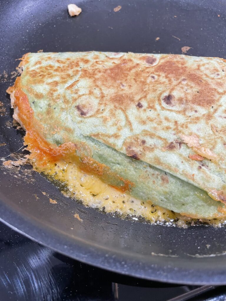 Golden brown Quesadilla with gooey cheese on pan.