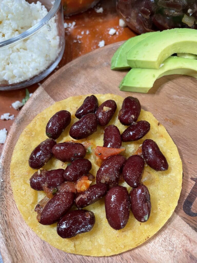 Added beans to corn tortilla on top of a wodden plate. Three slices of avocado 