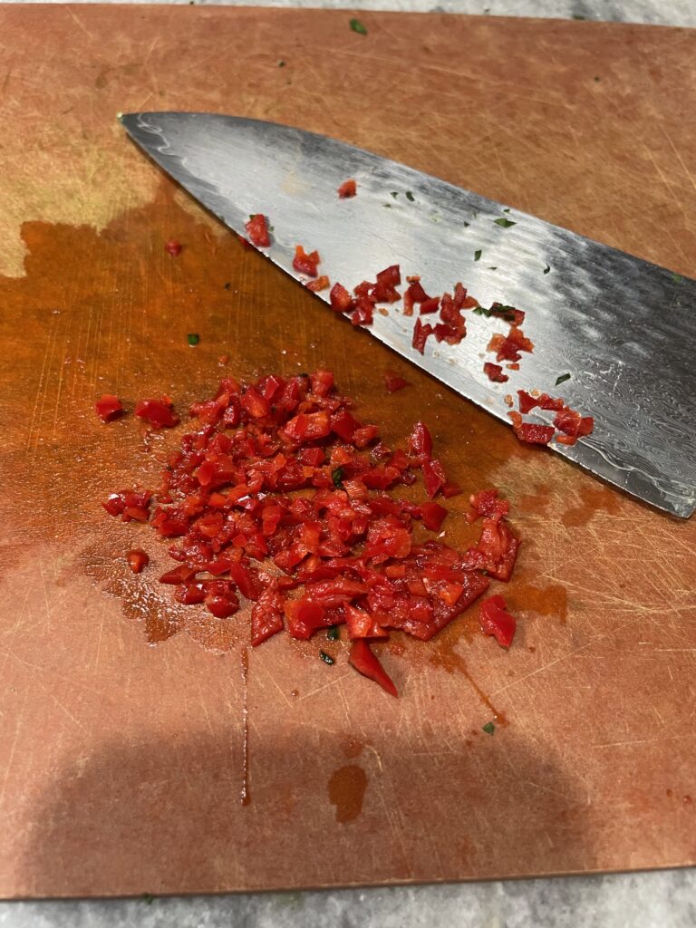 Minced red chili pepper on board. Knife next to it.