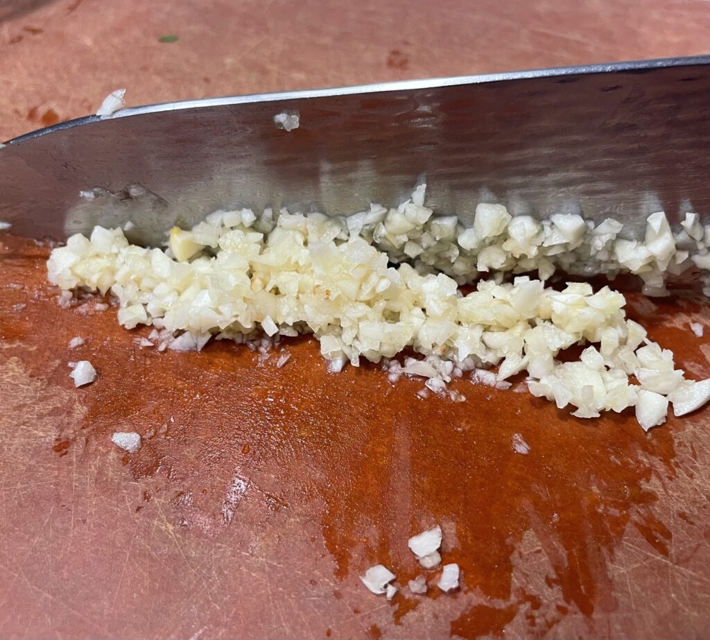 Minced garlic on a cutting board. With knife on the background. 